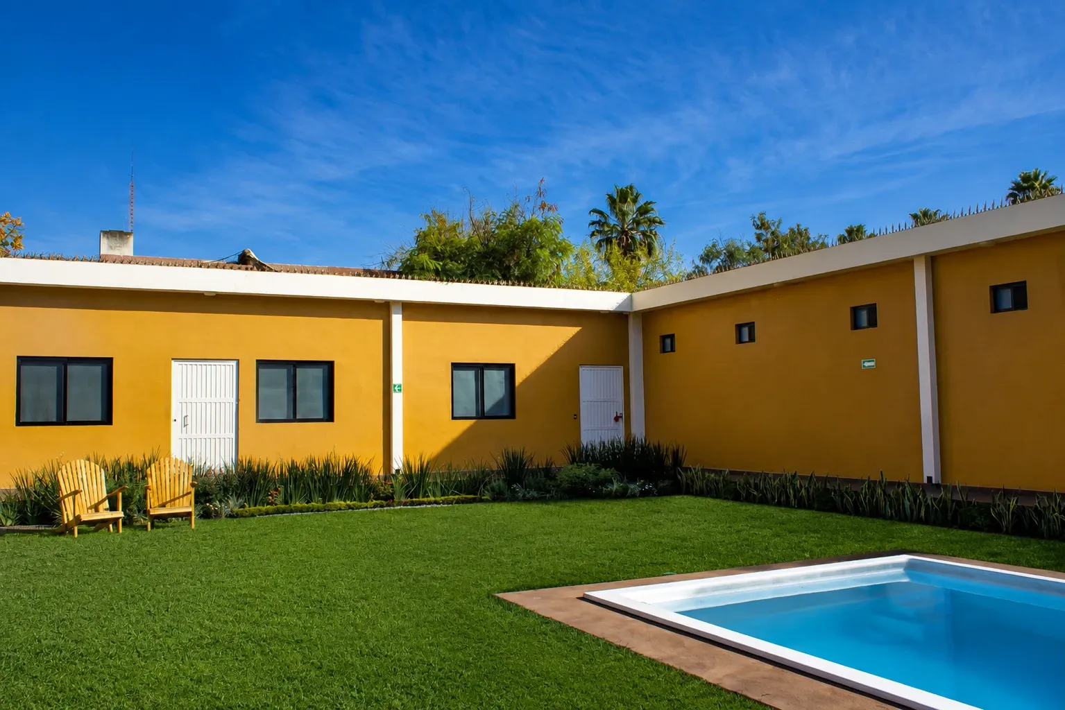 Garden and pool at the Lumenia house, with yellow walls and a blue sky