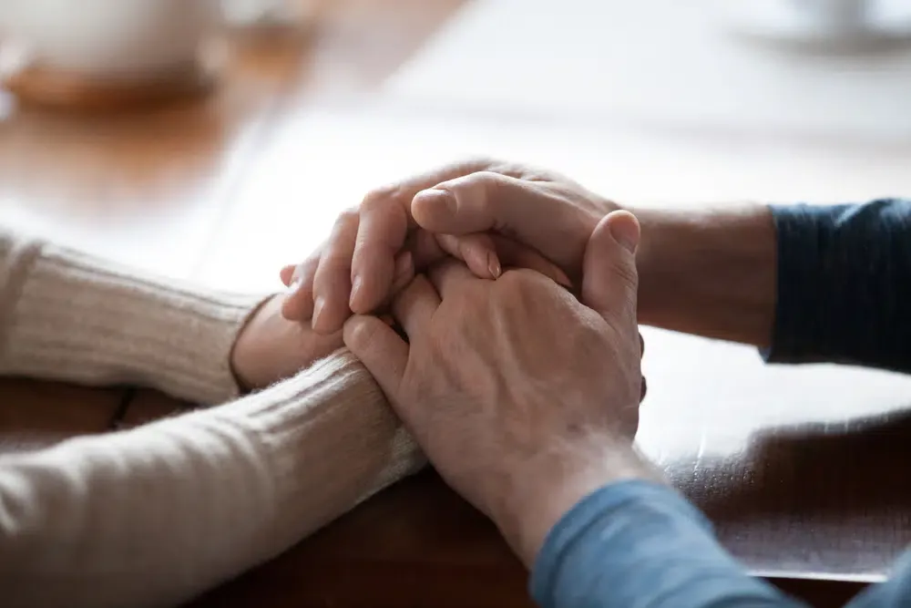 Two people holding hands across a table in a gesture of support